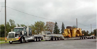 A large truck hauling a big machine down the street.