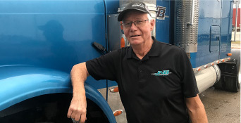 A man in a black shirt stands beside a blue truck.