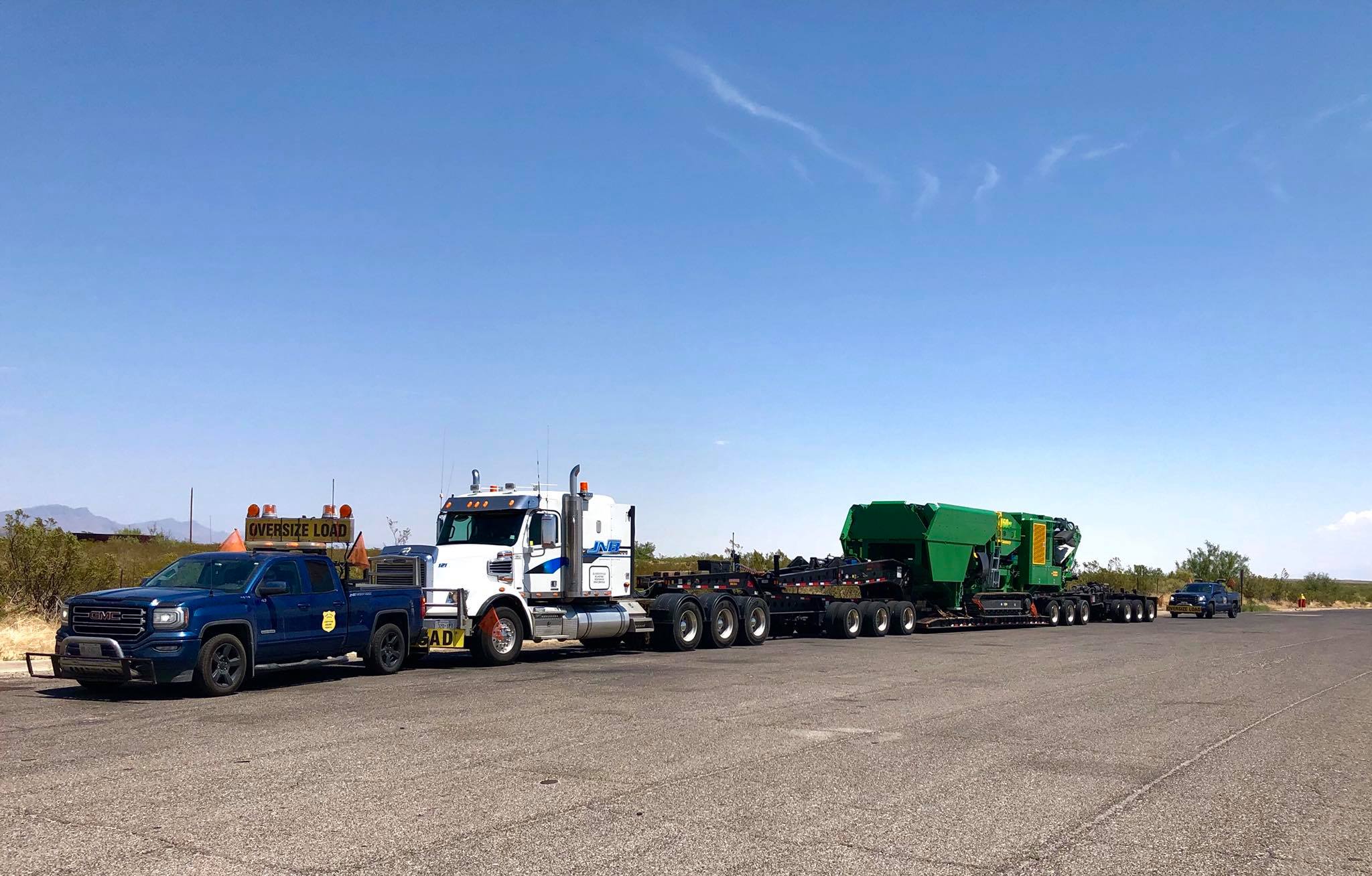 Two blue pickup trucks accompanying a large transport truck with oversized load signs.